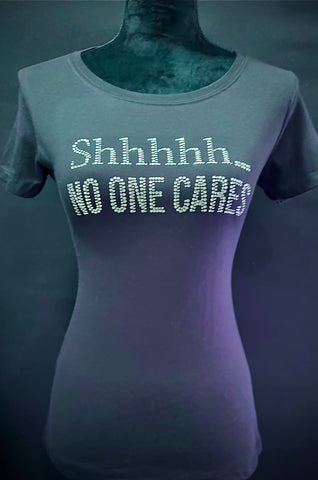 Black, round neck, fitted ladies T-shirt,  Embellished with rhinestone text graphic that says: Shhhh No one cares across  chest.  Wording in 2 lines.  Shhhhh... top line. No one cares--on 2nd line.  100% Cotton tee.