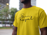 Clear image of yellow, round neck t-shirt on African American Male standing in front of blurred background scenery of building skyscraper and trees. Printed t-shirt has "Born Royal" in cursive graphic, centered horizontally across chest. 2 lines--Born on first line, Royal on second. T-shirt 100% cotton.