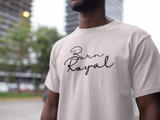 Clear image of white, round neck t-shirt on African American Male standing in front of blurred background scenery of building skyscraper and trees. Printed t-shirt has "Born Royal" in cursive graphic, centered horizontally across chest.  2 lines--Born on first line, Royal on second.  T-shirt 100% cotton.